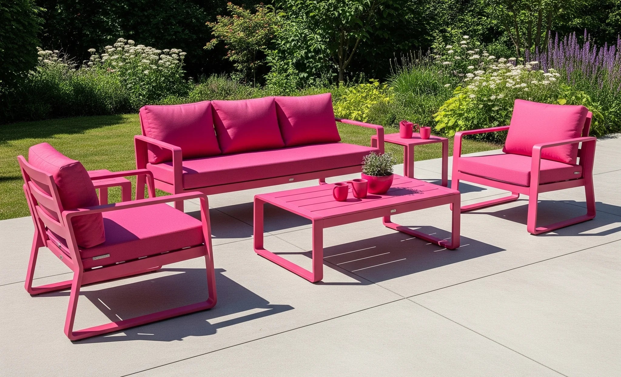 A sunny patio in Delhi features a vibrant hot pink sofa, chairs, and table. Lush green plants and a clear blue sky complete the bold outdoor living space.