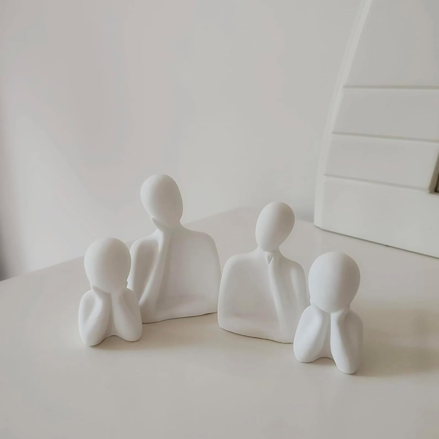Set of white abstract human-like sculptures on a light surface with a neutral background