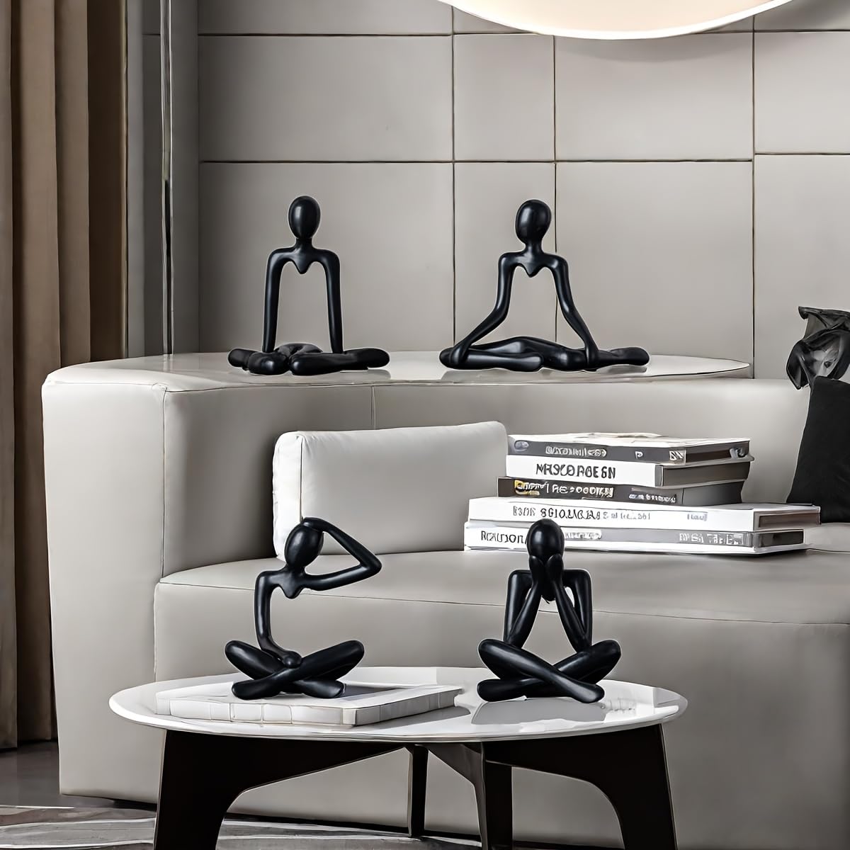 Black abstract sculptures on a white table and gray sofa with books in a modern interior setting.