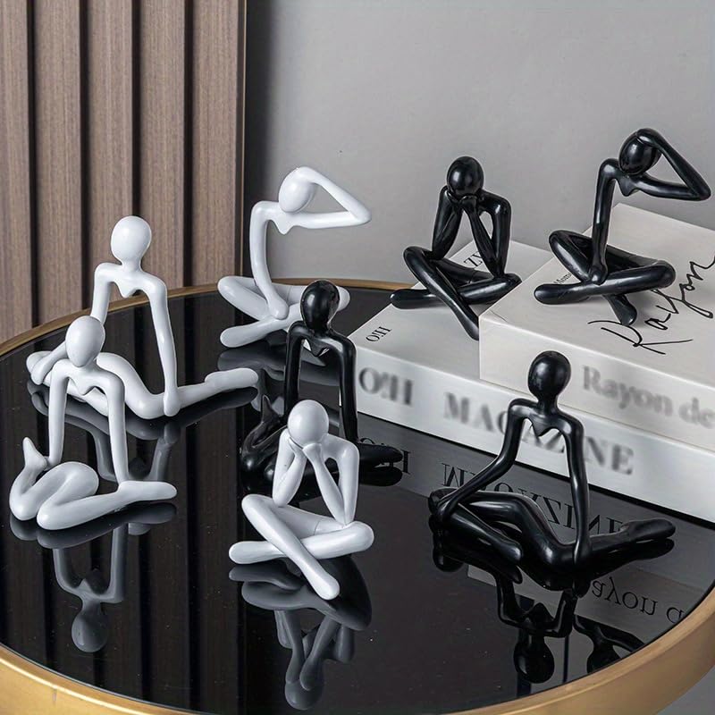 Black and white abstract figurines on a reflective surface with books in the background