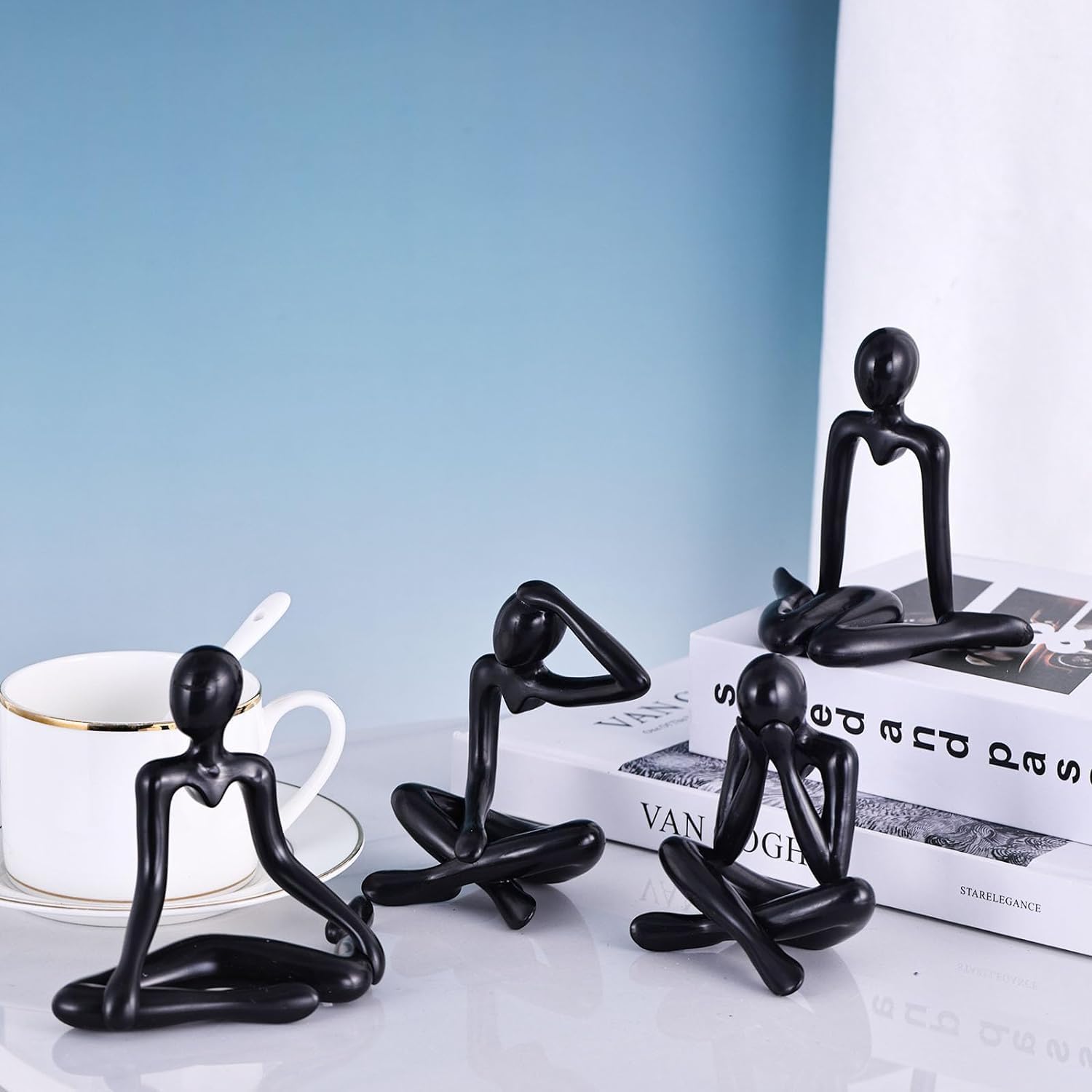 Set of black abstract figurines on a table with a cup and books in the background.