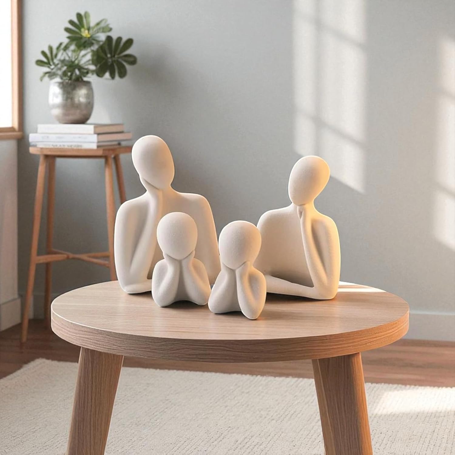 White abstract sculpture of a family on a wooden table with a plant and books in the background.