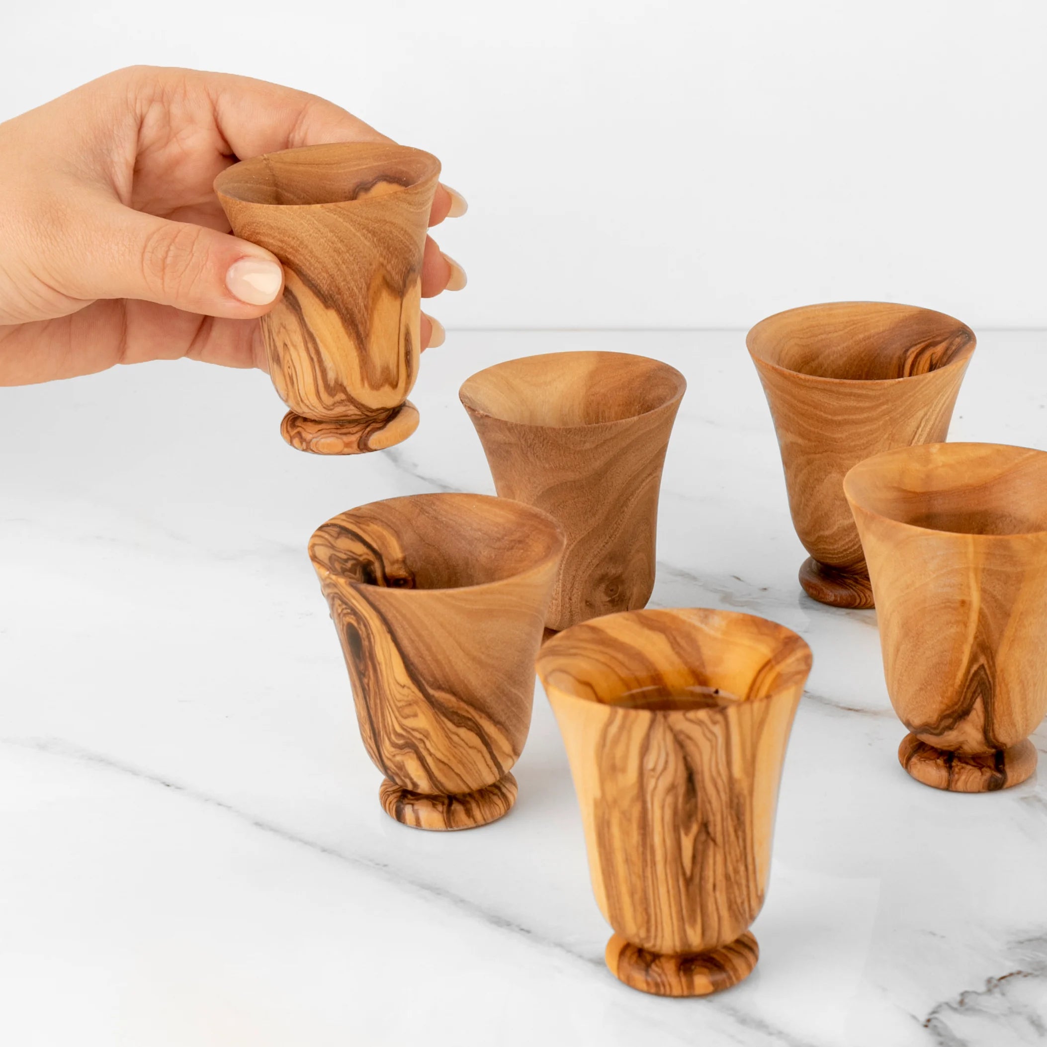 Wooden shot glasses on a marble surface with a hand holding one.