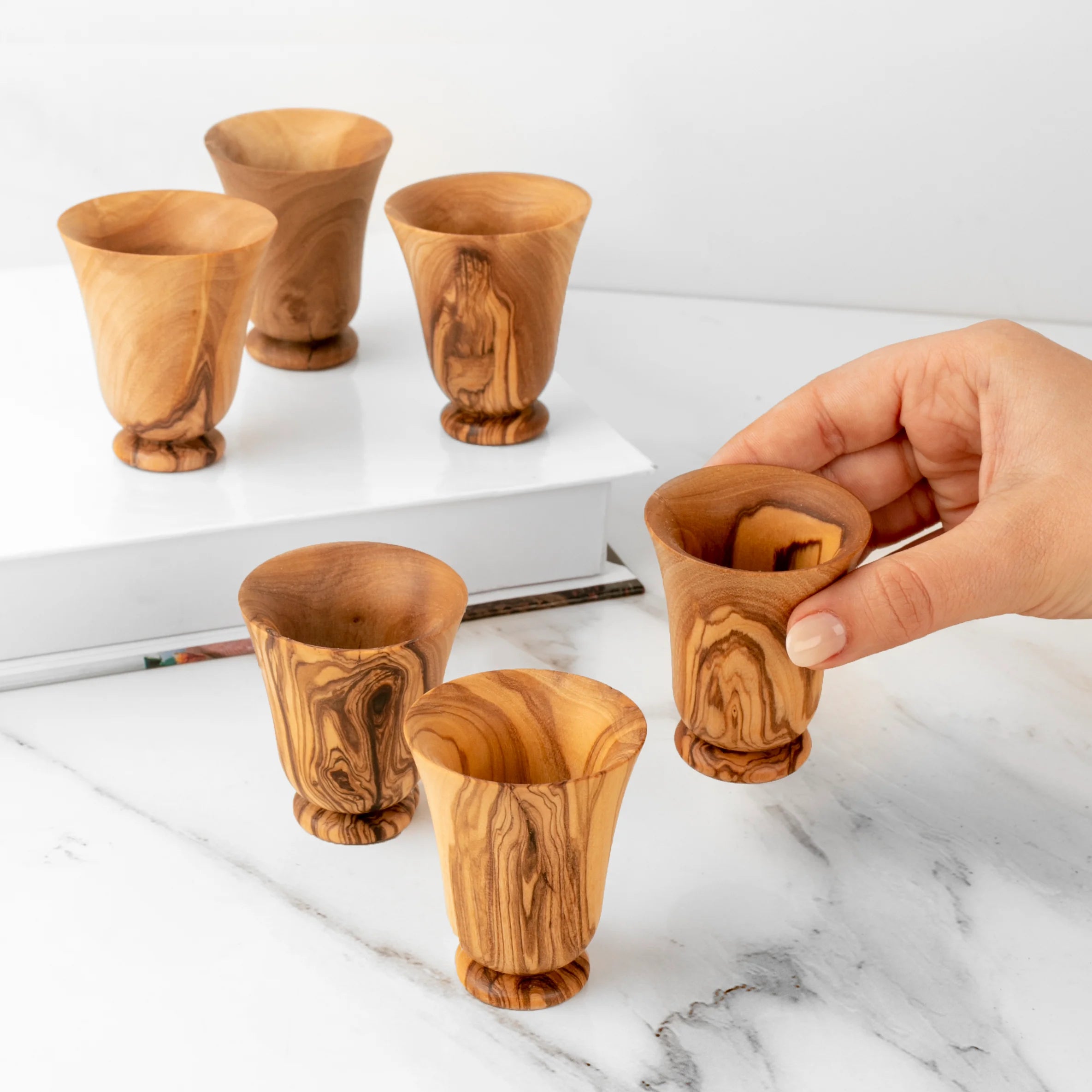 Set of wooden cups on a marble surface with a hand holding one cup.