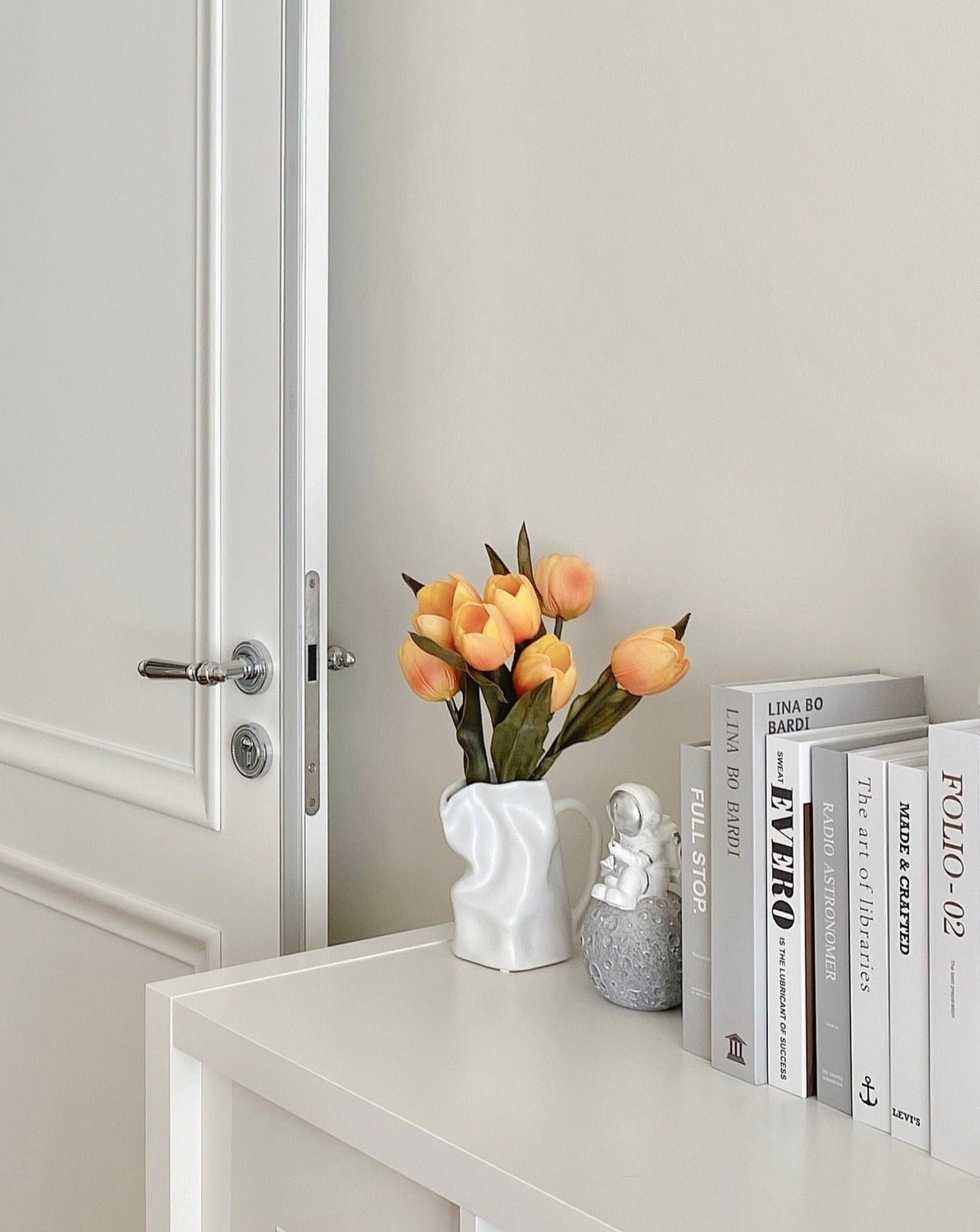 White cabinet with a vase of flowers, small statue, and books against a light gray wall.