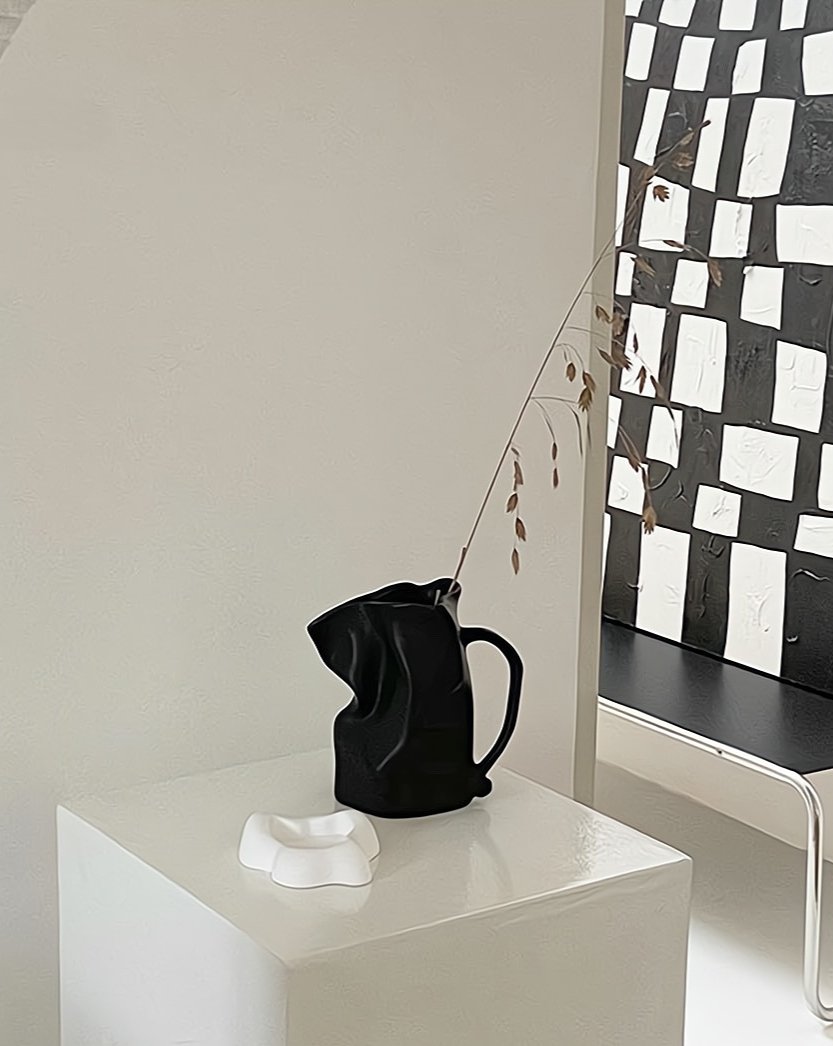 Black pitcher and white soap on a white surface with a patterned wall in the background
