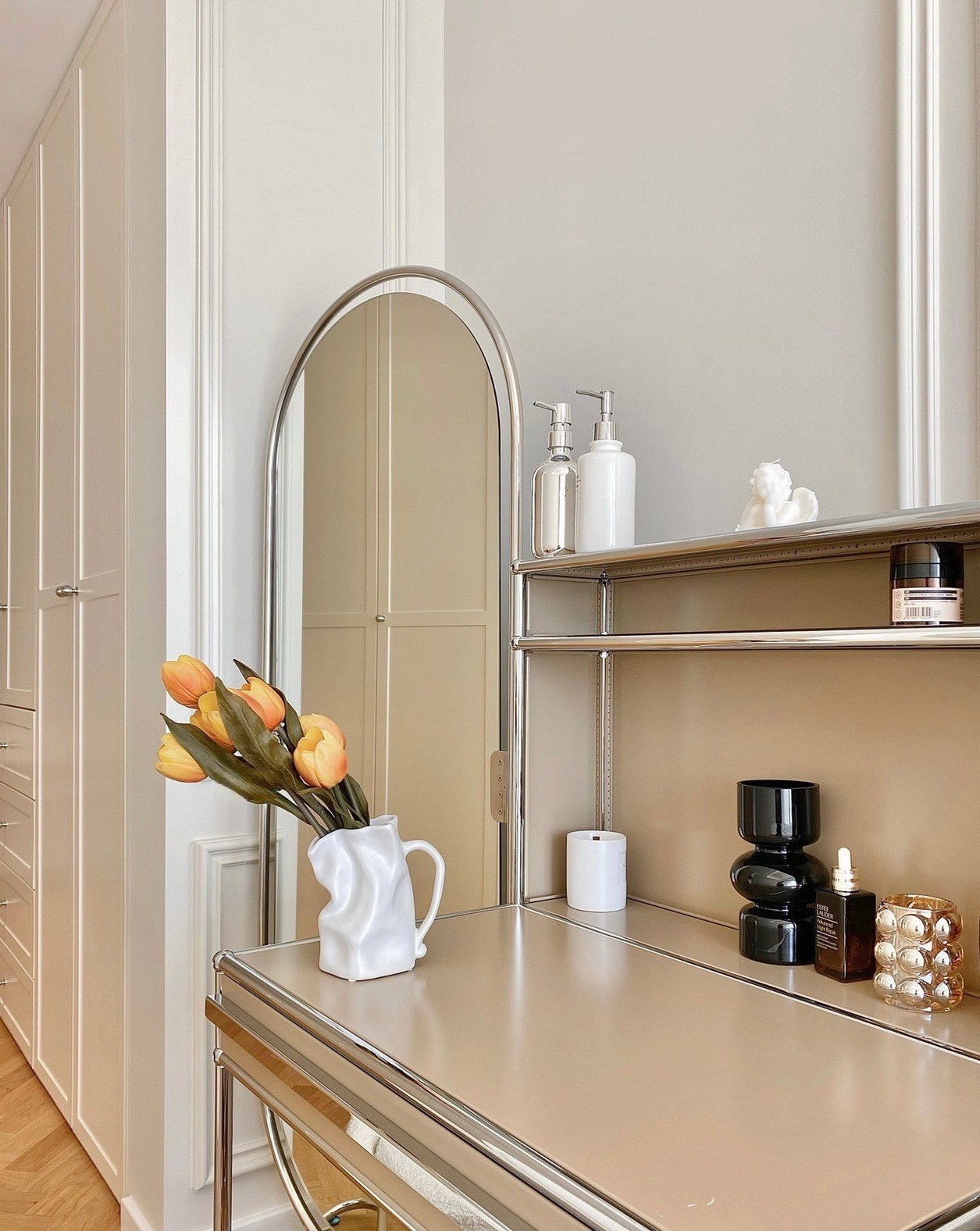 Beige vanity with mirror, flowers, and skincare products.