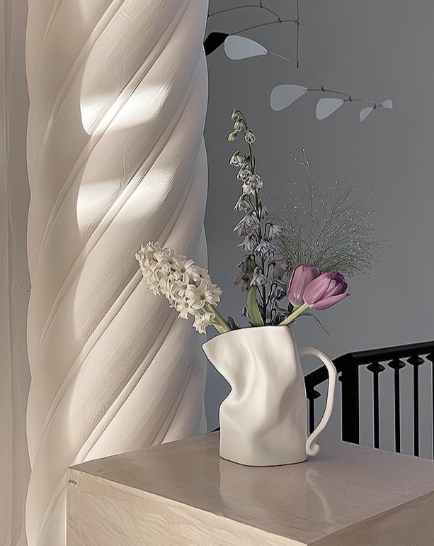 White pitcher with flowers on a table next to draped fabric